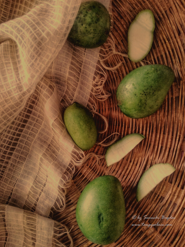 sliced and whole raw mangoes with white fabric and wood background