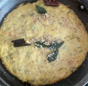 Handvo batter set in a pan with tempering of sesame seeds and curry leaves on top